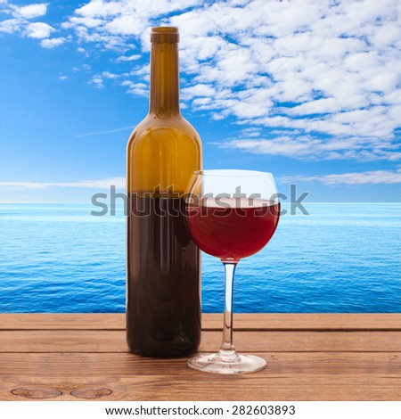 Glass of red wine and bottle on wooden background. Summer blurred background. Tropical landscape, sea. Flat mock up for design.