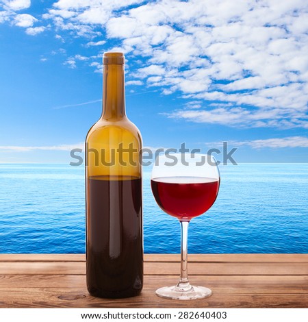 Glass of red wine and bottle on wooden background. Summer blurred background. Tropical landscape, sea. Flat mock up for design.