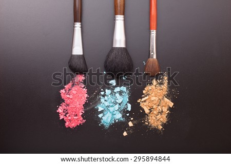 Makeup brushes on background with colorful powder. Crushed eyeshadow on black background. Abstract  background