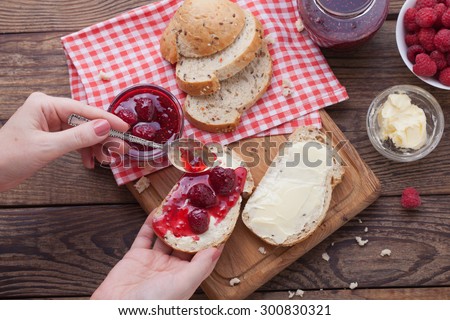 Strawberry jam, butter and bread on wooden table. Breakfast with strawberry jam top view horizontally. Macro shot selective focus. Woman smears bread butter and jam.