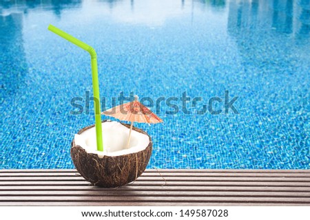 coconut cocktail with green drinking straw and cocktail umbrella by the swimming pool