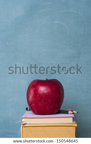 books apple and pencil in front of green chalkboard