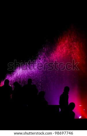 Silhouettes of People watching colorful fountain light show at night