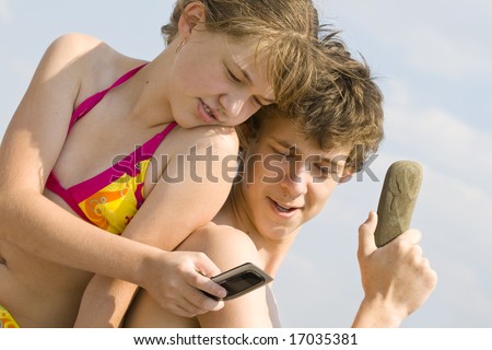 The girl talks by a mobile phone, the guy speaks on the phone from a stone
