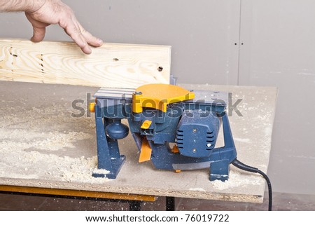 Close-up of a construction worker\'s hand and power tool while planing a piece of wood trim for a project.