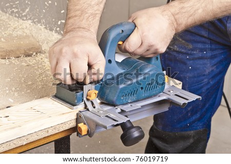 Close-up of a construction worker\'s hand and power tool while planing a piece of wood trim for a project.