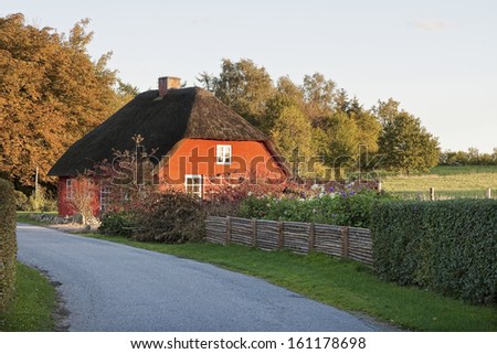 Small red house with thatched roof in the sunset. Copy space.