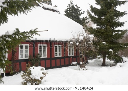 Red half-timbered house with snow on the thatched roof