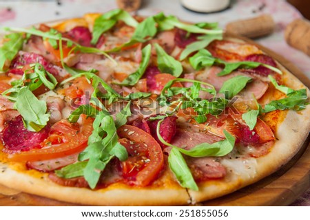 Close up Italian pizza with bacon, salami, tomatos and rocket salad on the wooden plate