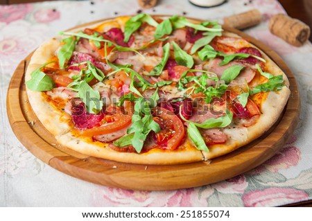 Italian pizza with bacon, salami, tomatos and rocket salad on the wooden plate