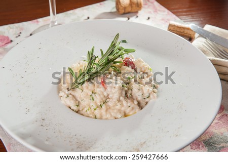 Close up Delicious italian risotto with white mushrooms, tomatoes and parsley decorated with rosmary and parmesan on the white plate