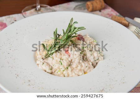 Close up Delicious italian risotto with white mushrooms, tomatoes and parsley decorated with rosmary and parmesan on the white plate