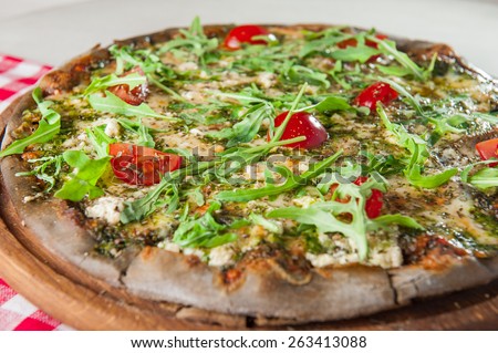 Traditional Vegetarian Italian pizza with vegetables, tomato sause,cheese, rocket salad and dried basil on the wooden plate close up