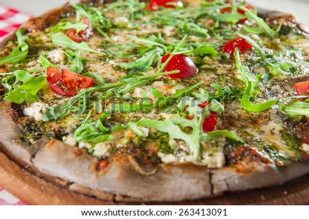 Traditional Vegetarian Italian pizza with vegetables, tomato sause,cheese, rocket salad and dried basil on the wooden plate close up