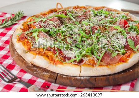 Close up Traditional Italian pizza Parma with bacon, tomatos and rocket salad on the wooden plate