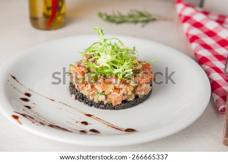 Closeup Raw salmon tartare with mixed vegetables decorated with lettuce mix on the white plate. Gourmet Food