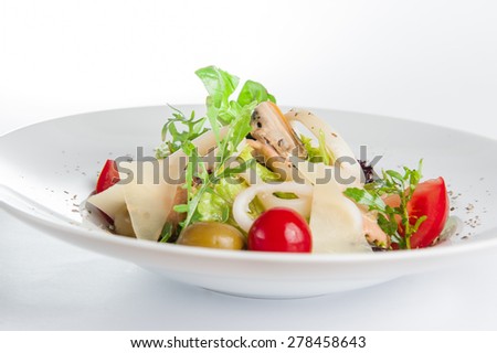 Close up Seafood Salad with squid, mussels, parmesan cheese, lettuce, mix olives, arugula, tomatoes, decorated with a sprig of basil on white plate isolated on white background