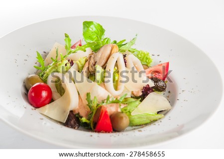 Close up Seafood Salad with squid, mussels, parmesan cheese, lettuce, mix olives, arugula, tomatoes, decorated with a sprig of basil on white plate isolated on white background