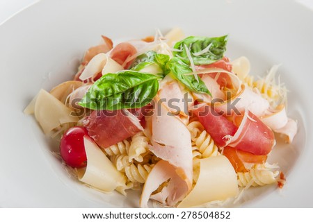 Close up  Plate of meat Pasta with ham and  prosciutto slices decoratred with cherry tomatos, parmesan cheese and basil on the white plate isolated