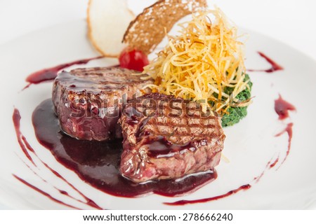Restaurant serves meat steak with spinach pillow and potato\'s brushwood in berry sauce, garnished with breadcrumbs and cherry tomatoes on white plate isolated