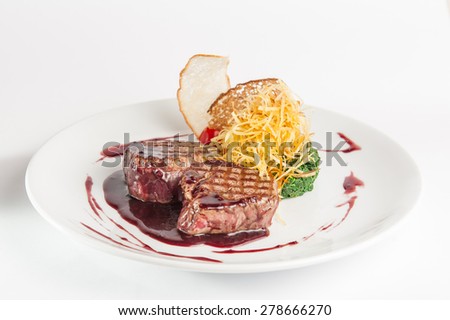 Restaurant serves meat steak with spinach pillow and potato\'s brushwood in berry sauce, garnished with breadcrumbs and cherry tomatoes on white plate isolated