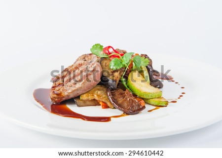 Restaurant serves meat steak with stewed vegetables and sauce: zucchini, eggplant, carrots, mushrooms, decorated with herbs and spices on white plate isolated
