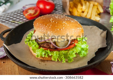 Close up tasty Burger with  beef meat, cheese, lettuce and vegetables  in the pan on the table  arounded some ingredients