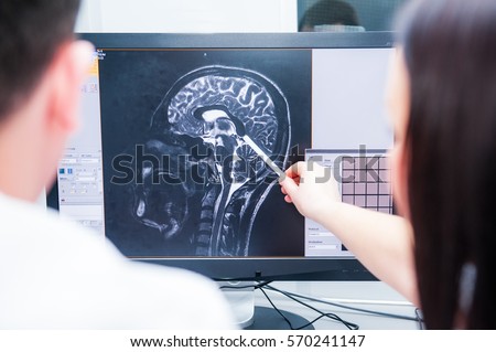 Doctors consider and discuss magnetic resonance image (MRI) of the brain. Back view, selective focus