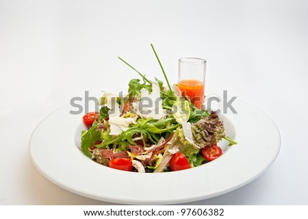 Delicios Italian Salad mix with chicken breast, bacon, tomatoes cherry, arugula, lettuce and sliced parmesan served with carrot sauce in the round white plate isolated on the white background