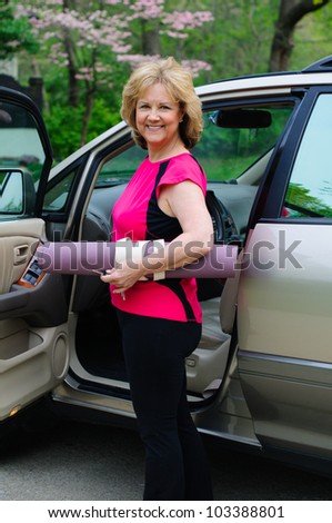 An attractive older woman holds a yoga mat under her arm as she gets into a car.