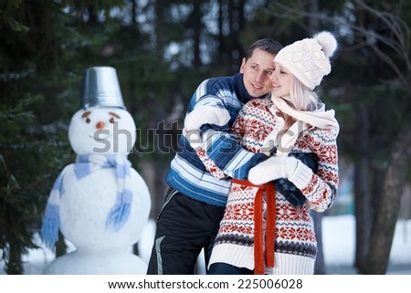 Young couple in knitted hats and sweaters to have fun and laughs next to the snowman