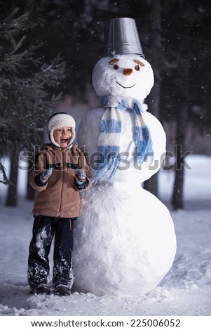 Winter. The boy laughs, standing next to a snowman.Carrots instead of the nose, the bucket on his head.