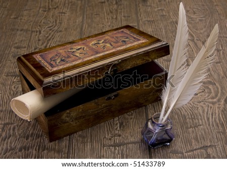 The ancient chest with a paper inside stands on a table near to a feather and ink