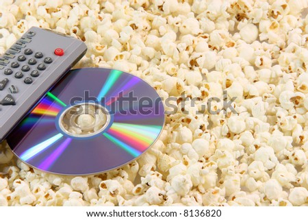 television remote control and dvd disc movie on pop corn background food and entertainment concepts