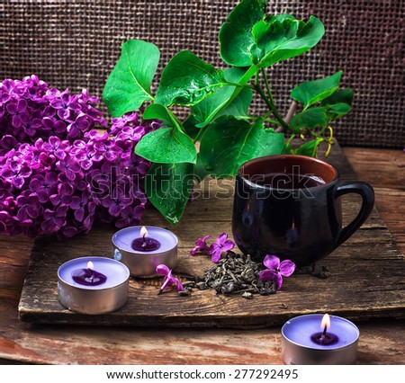Cup of tea,three candles,branch of blossoming lilac on wooden surface