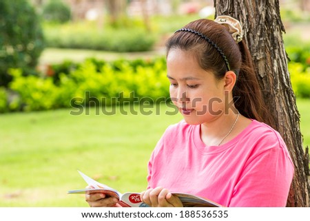 Asian woman reading travel magazine book in park.