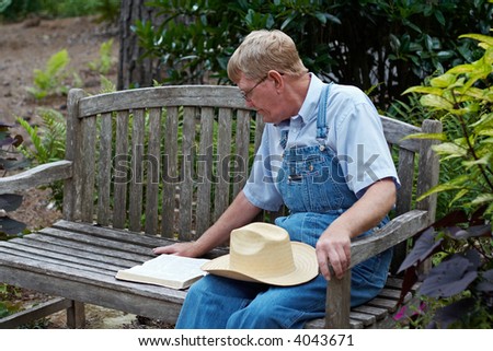 An older man studying the Bible outside on a bench.