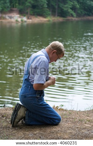 A man on his knees praying beside a lake.