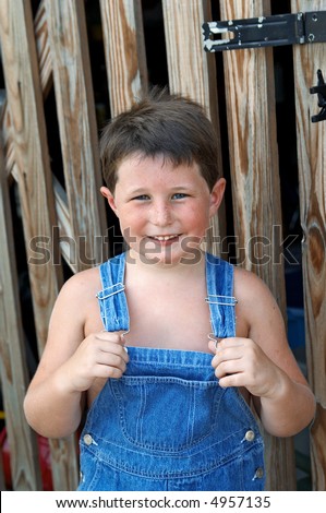 stock photo : A six year old boy in overalls standing in front of a barn door.