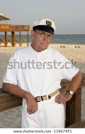 An older man wearing a captains hat at the beach.