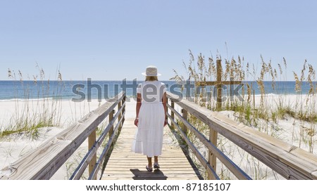 A woman walking on a boardwalk nest to a cross at the beach.