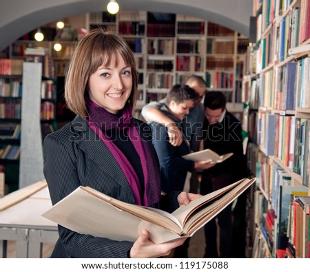 Smiling female student holding book. Students in the background.