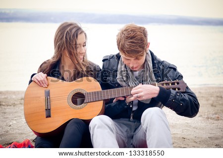 Young girl with acoustic guitar and her boyfriend on the beach
