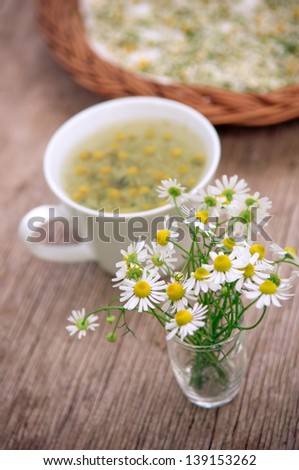 Camomile flowers and whithe cup of tea on wooden surface