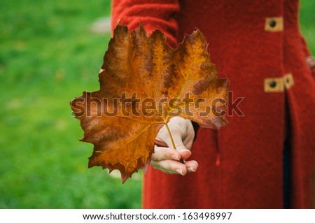 Woman in red coat holding yellow leaf