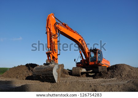 Orange excavator at work in open sand mine and a blue sky