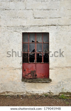 Red metal window frame with broken glass in a white stone wall