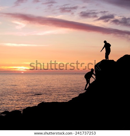 Climbing silhouette at rocky seashore gets a helping hand to get up during sunset in Brittany, France