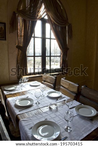 dining table with crockery on a white tablecloth near the window with curtains
