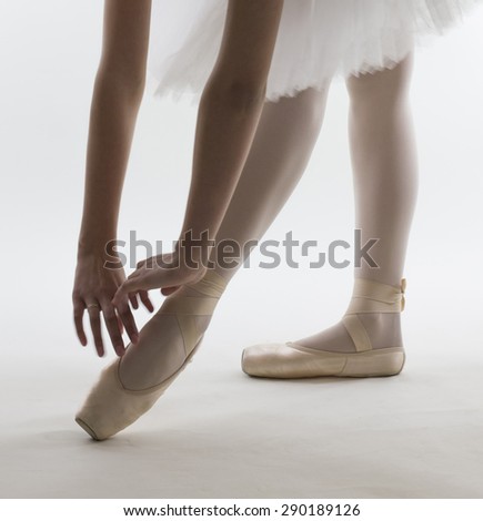 Young ballerina in white ballet tutu is dancing on a white background